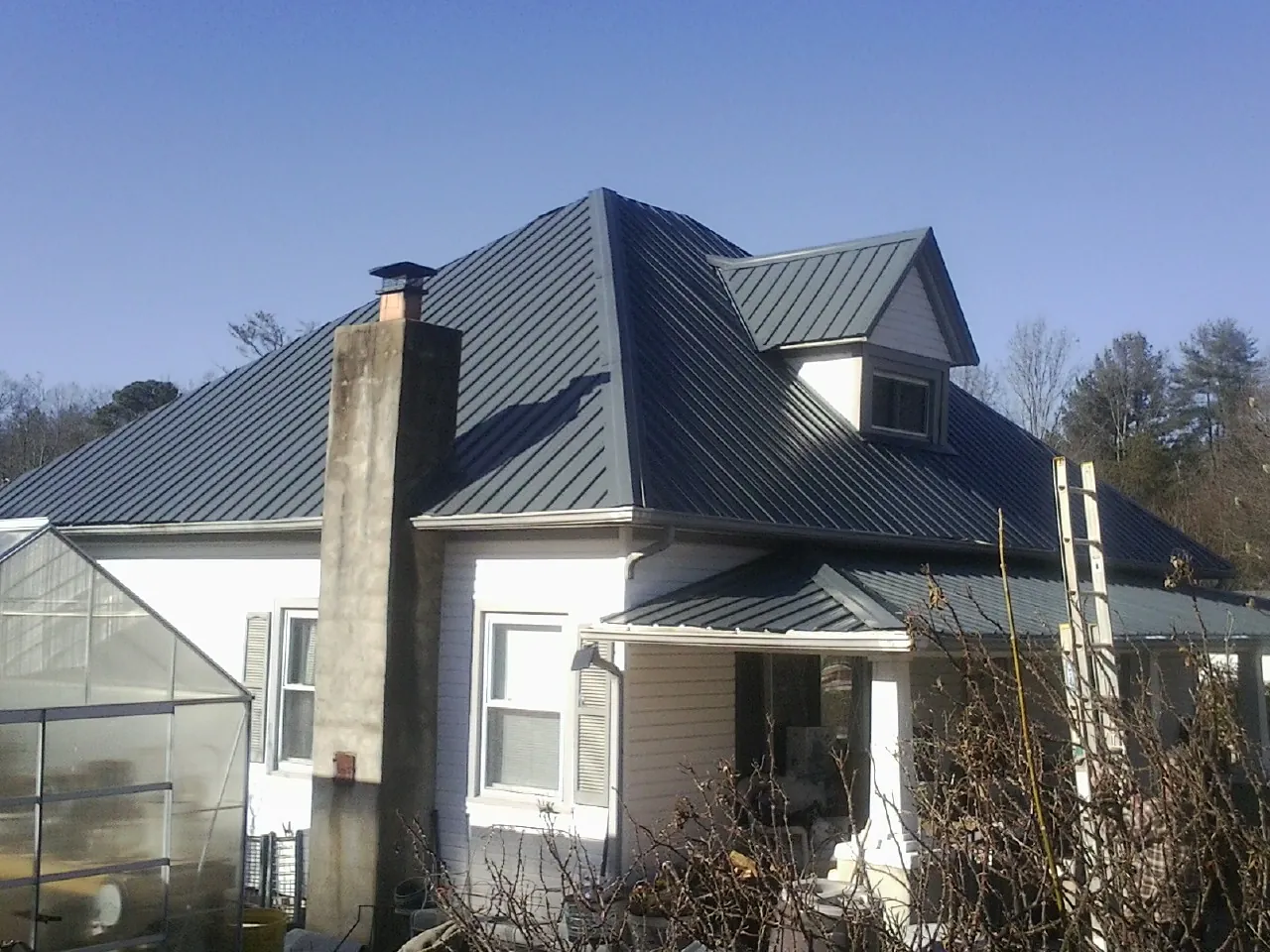 Dark blue standing seam metal roof on a white farmhouse with dormer — Slate & Tile Roof Repair by Roofing Brothers in Lafayette