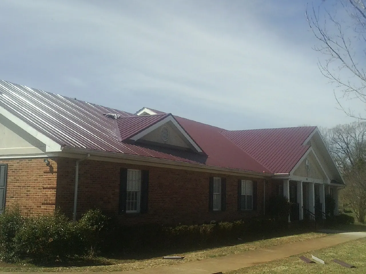 Red metal roof with gabled entries on a long brick building, from a Hail Damage Roof Repair job in Lafayette